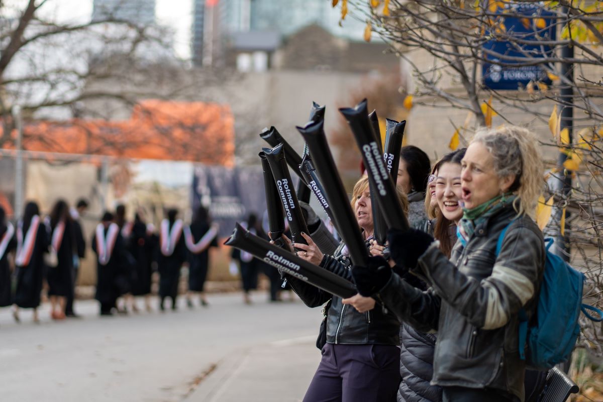 A line of people with thunder sticks cheering on another line of graduating students in robes.