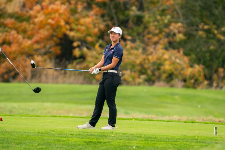 Varsity athlete Mia Wong holds a golf club and smiles on the green.